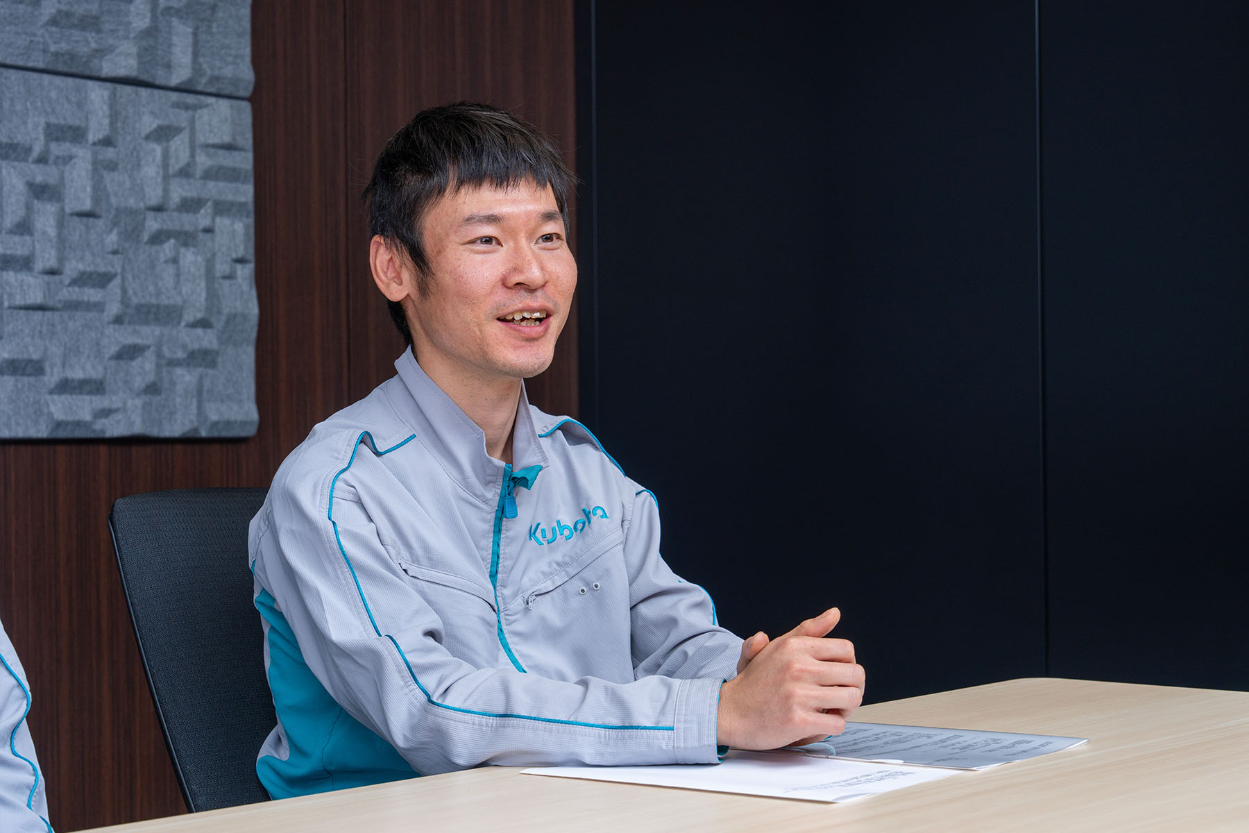 Tatsuya Kamada answers interview questions with a smile in a conference room.
