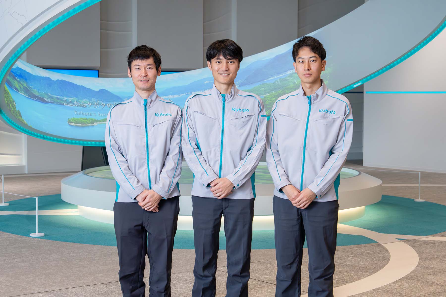 Yutaro Yoshida, Tatsuya Kamata, and Ginji Matsuoka  are photographed standing in front of a sculpture in the building entrance.